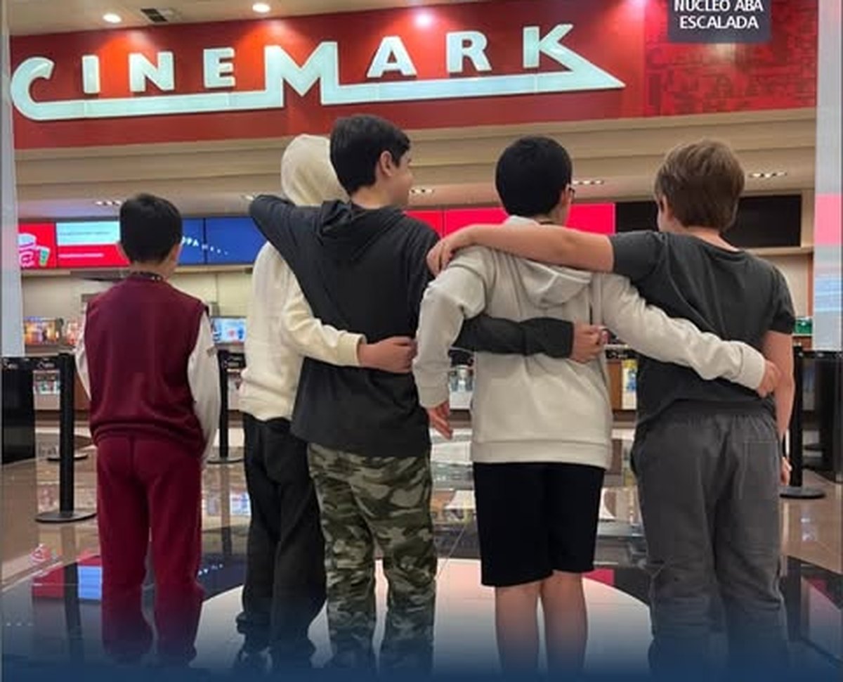 Grupo de participantes das Habilidades Sociais da Clínica Escalada, fotografados de costas e abraçados, diante da entrada de um cinema